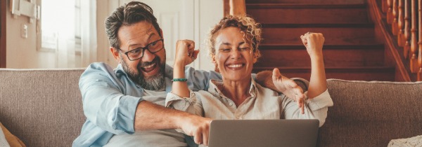 Mann und Frau sitzen vor dem Laptop und jubeln.
