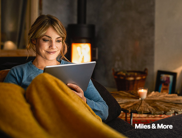 Frau liegt mit ihrem Tablet auf dem Sofa. Jetzt mit Cash & Miles 40 % deiner Meilen im vergleich zum regulÃ¤ren Meilenwert sparen.