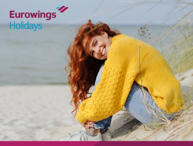 Frau mit roten Haaren sitzt am Strand. Jetzt Black Week Deals von Eurowings Holidays sichern.