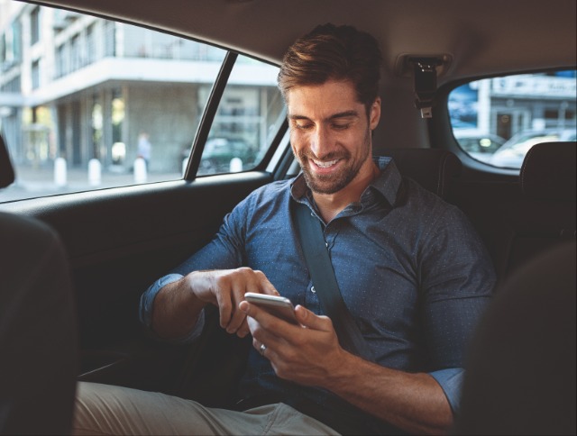 Man sitzt im Auto und schaut auf sein Handy. Jetzt Meilen sammeln.