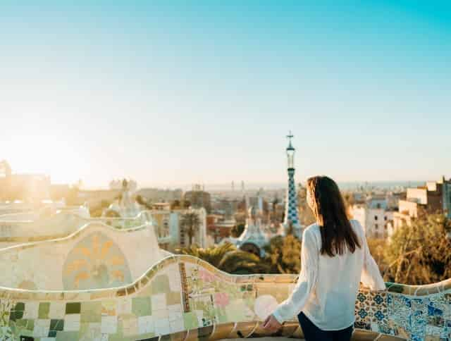 Eine Frau steht im Park Güell und überblickt das Häusermeer von Barcelona – jetzt Citytrip buchen und mit unseren Aktionscodes sparen!