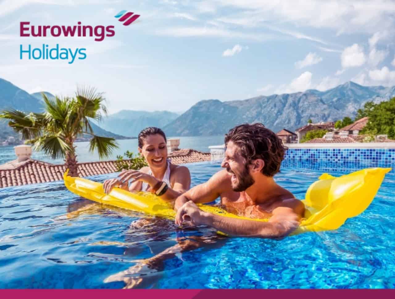 Eine Frau und ein Mann albern ausgelassen in einem Pool vor sommerlicher Kulisse herum. Jetzt Last-Minute-Urlaub buchen.